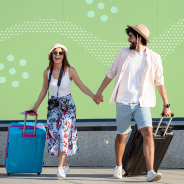 Couple in summer clothing holding hands while pulling rolling luggages