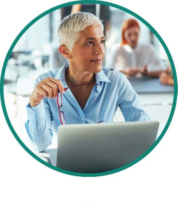 A woman in her 50s works on a laptop in an office environment