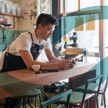 A man leaning on a bar, looking at a tablet screen