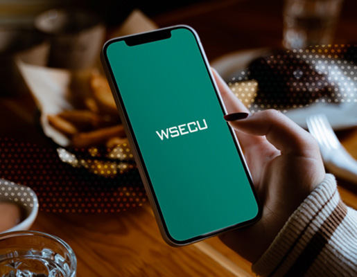 Close-up of a smartphone showing the WSECU screen, held over a table with food and drinks.