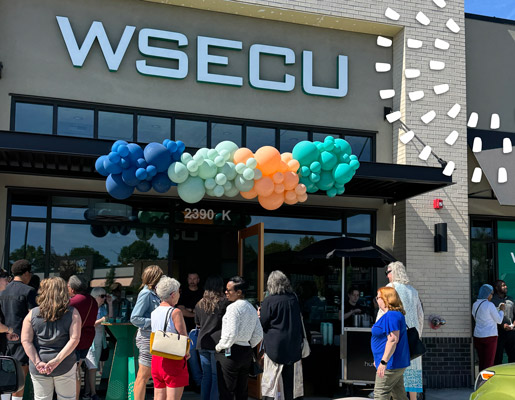 People gathered outside the WSECU Hawks Prairie branch beneath a colorful balloon arch at the entrance.